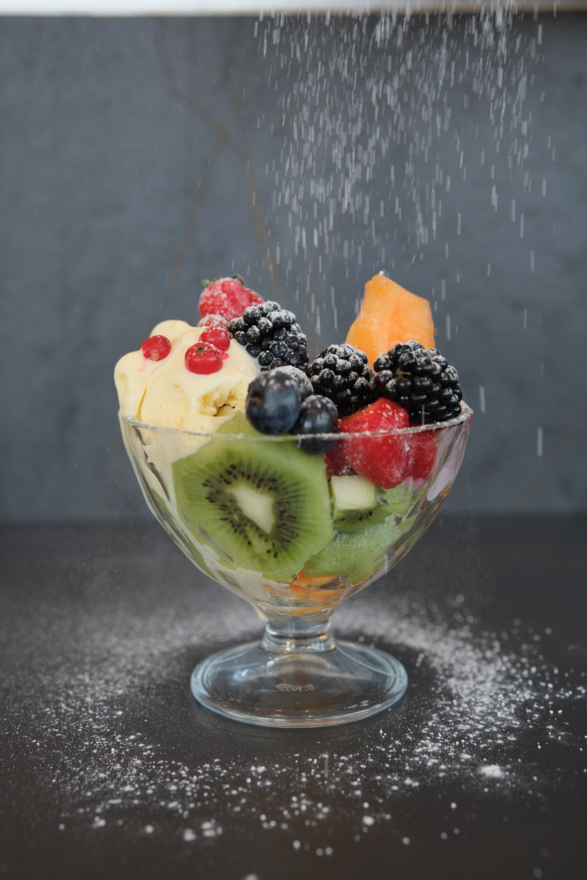Coppa gelato alla frutta con frutti di bosco, kiwi e melone, spolverata con zucchero a velo.
