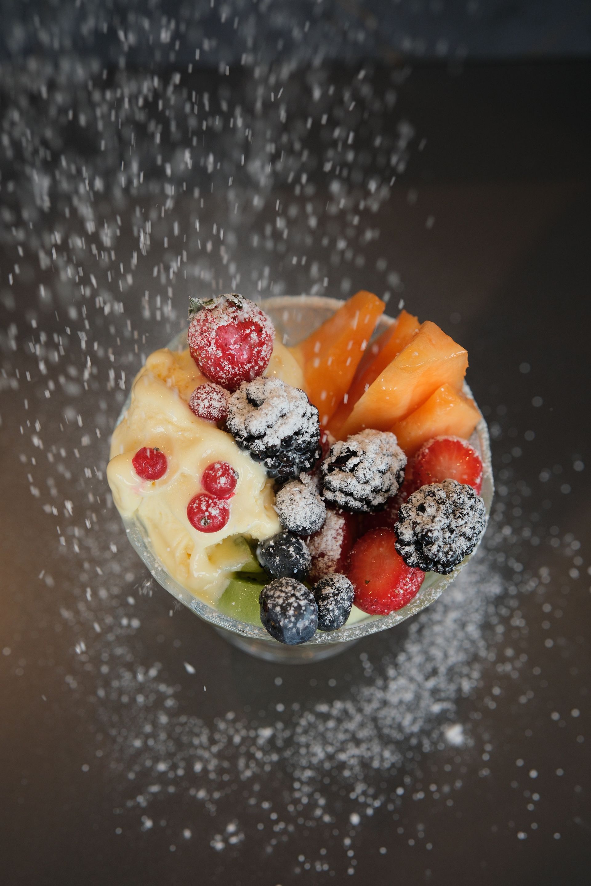 Dessert di frutta con spolverata di zucchero a velo su sfondo nero.