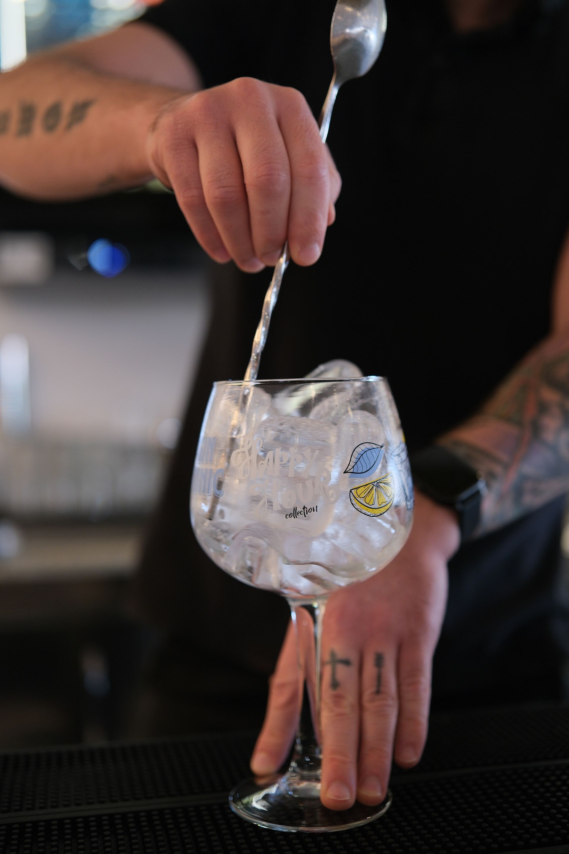 Barista che mescola un gin tonic in un bicchiere a tulipano con ghiaccio, ambiente da bar.