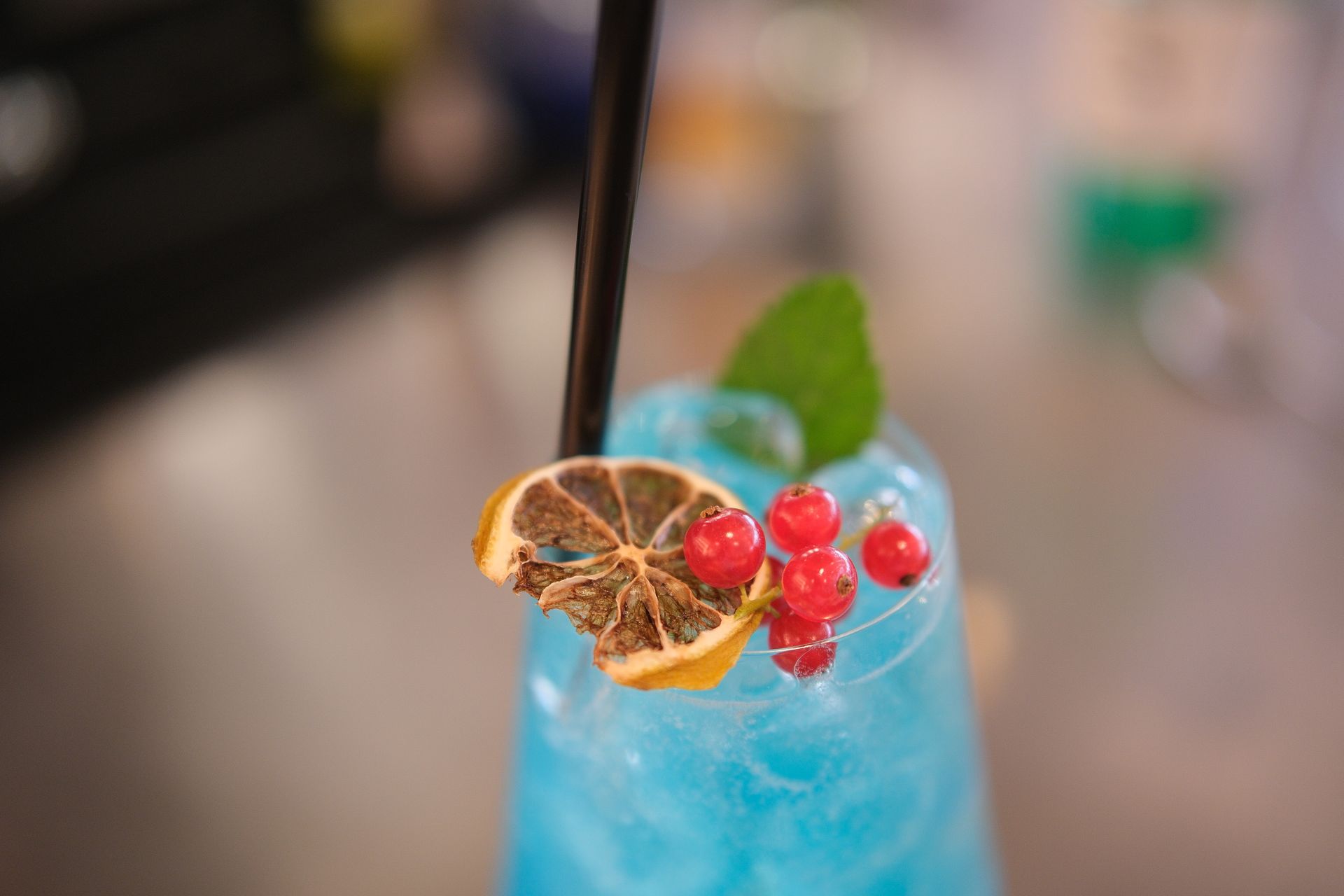 Cocktail blu con ghiaccio, guarnito con frutti di bosco, fetta di limone e menta.