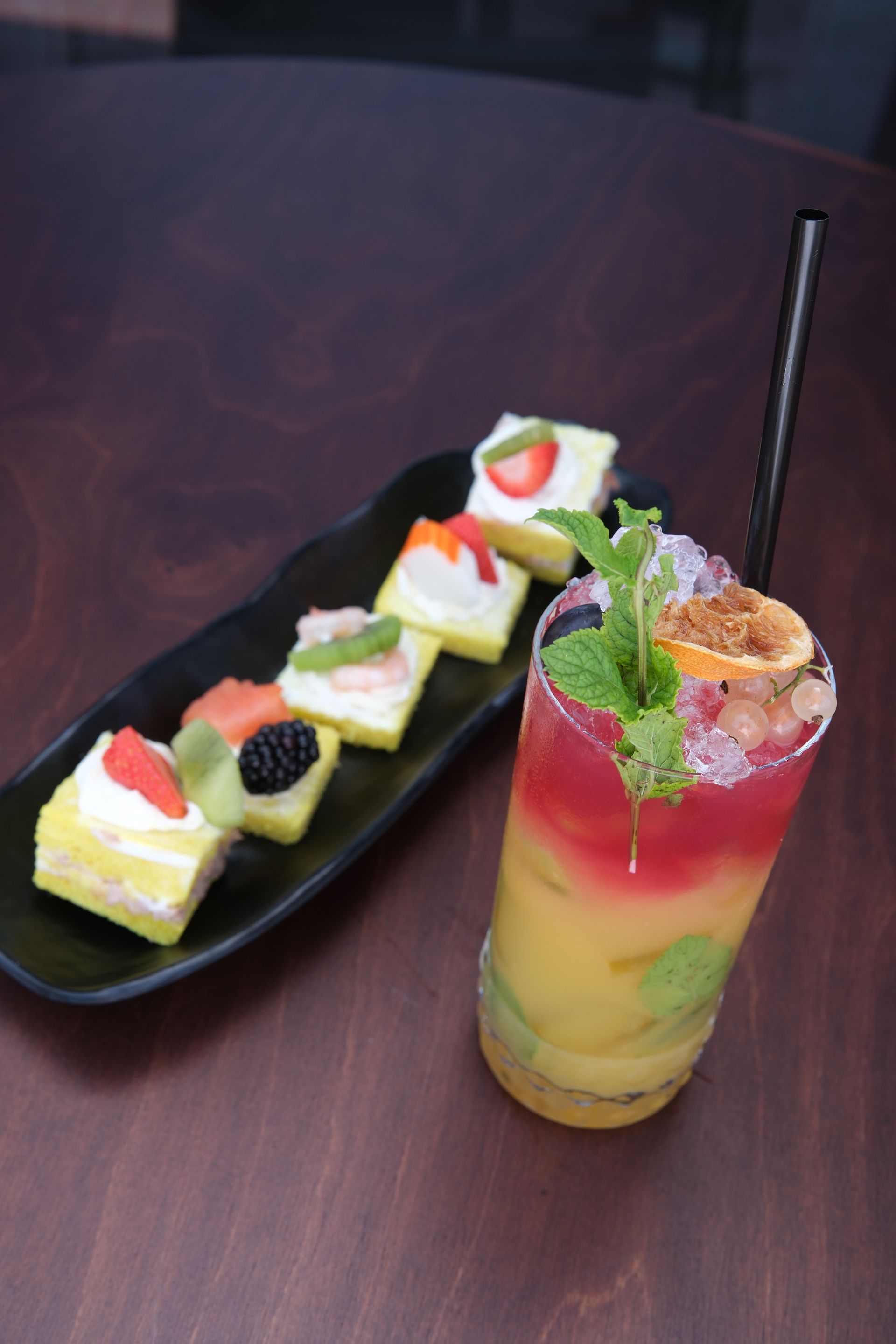 Cocktail con strati di colori, guarnizione di menta e stuzzichini colorati su un tavolo di legno scuro.