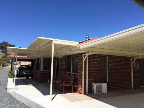 A car is parked under a canopy in front of a brick house.