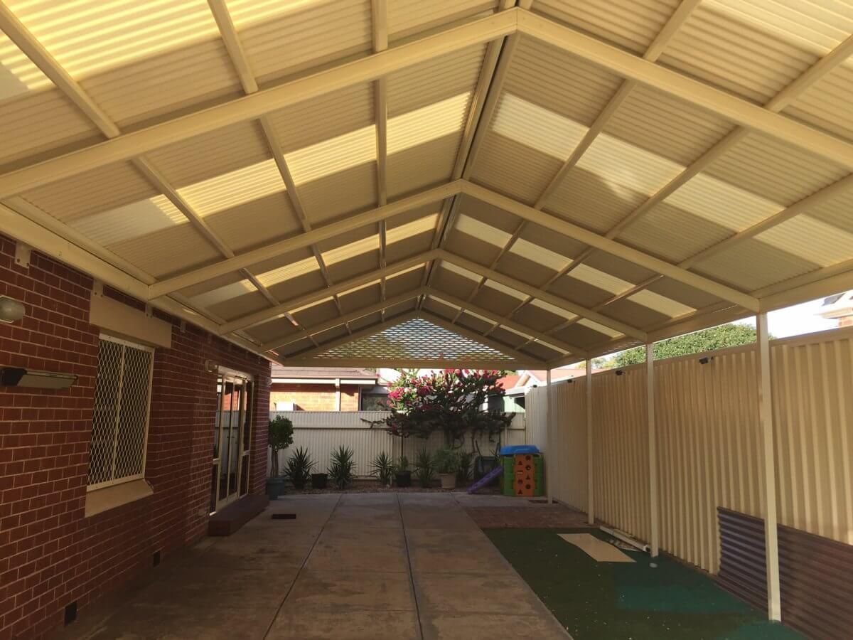 A carport with a clear roof and a brick house in the background.