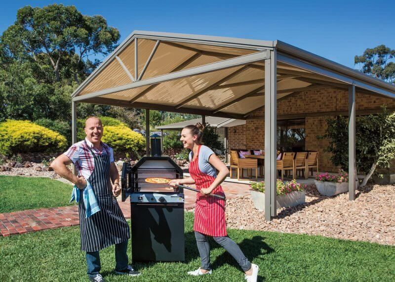 A man and a woman are standing next to a grill under a canopy.