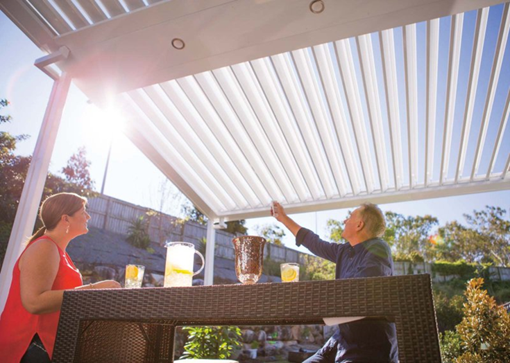 A man and a woman are sitting at a table under a pergola.