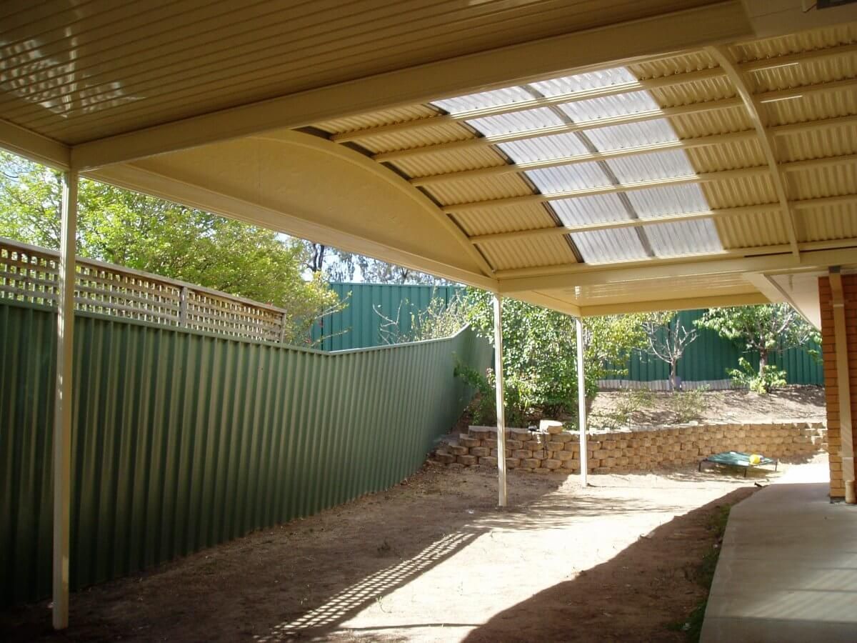 A carport with a clear roof and a green fence in the background