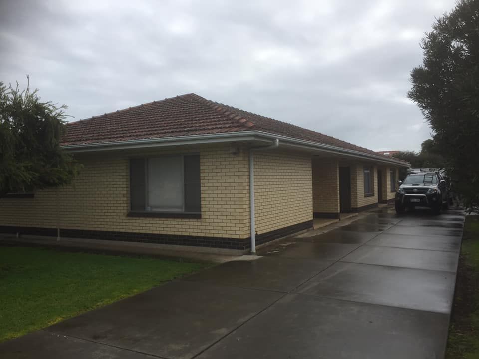 A brick house with a car parked in front of it on a rainy day.
