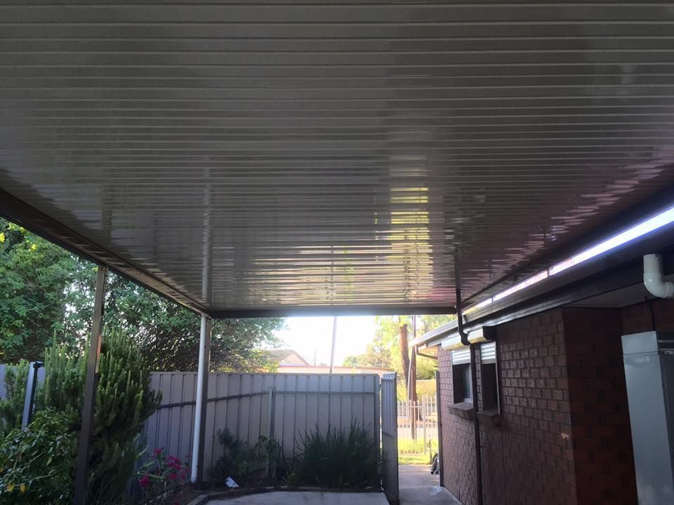 A carport with a white ceiling and a brick building in the background.