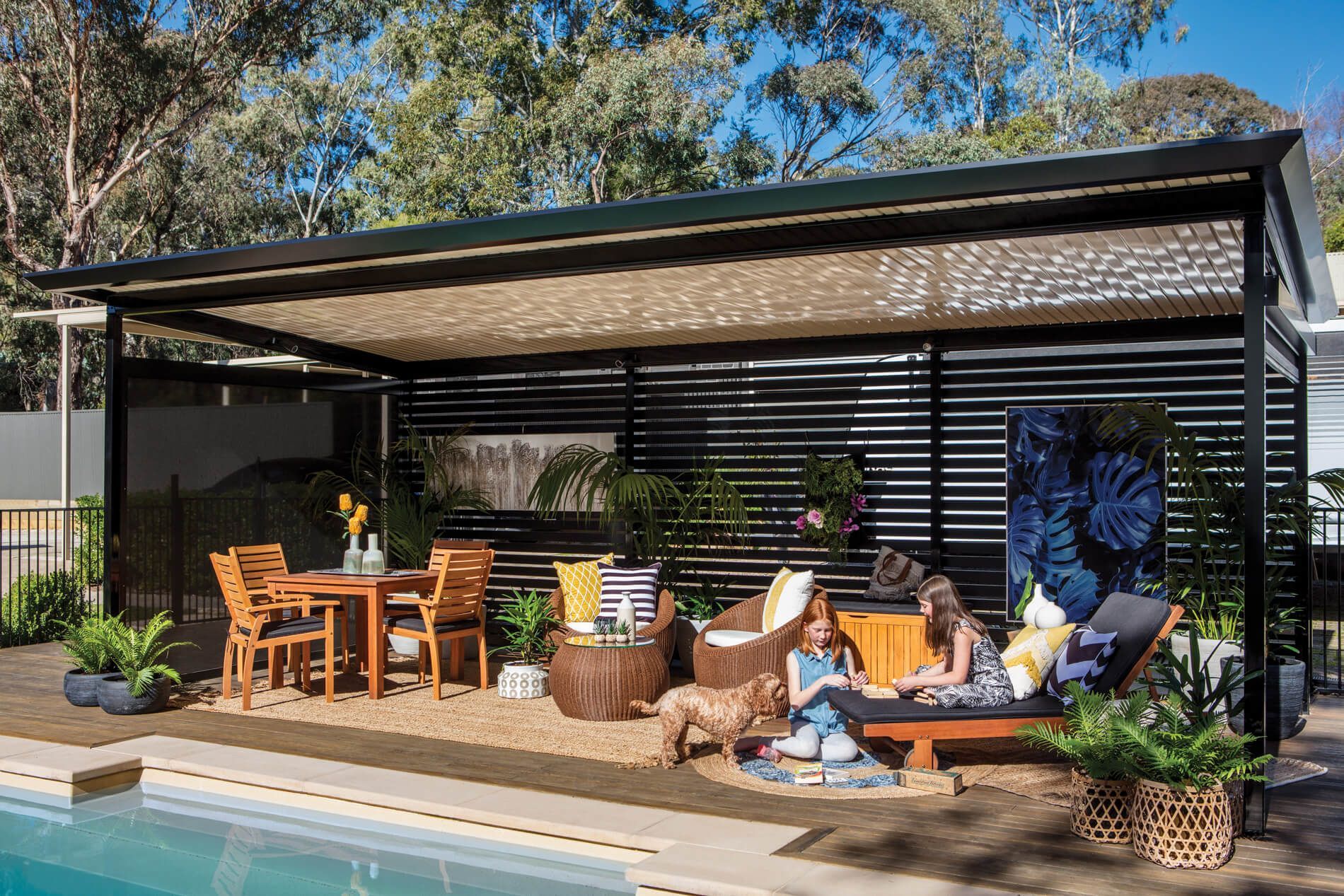 A woman and a child are sitting under a pergola next to a swimming pool.