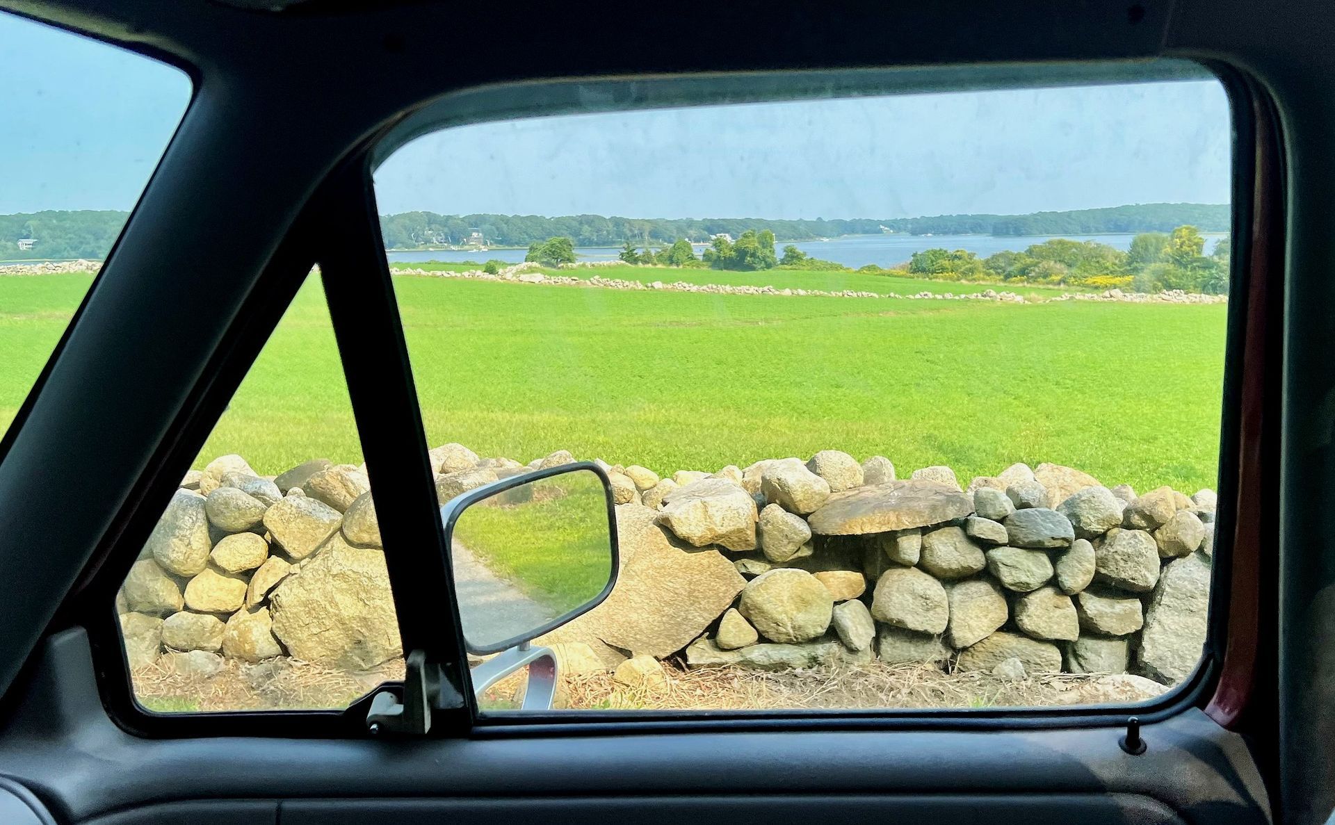 A car window with a view of a field and a stone wall