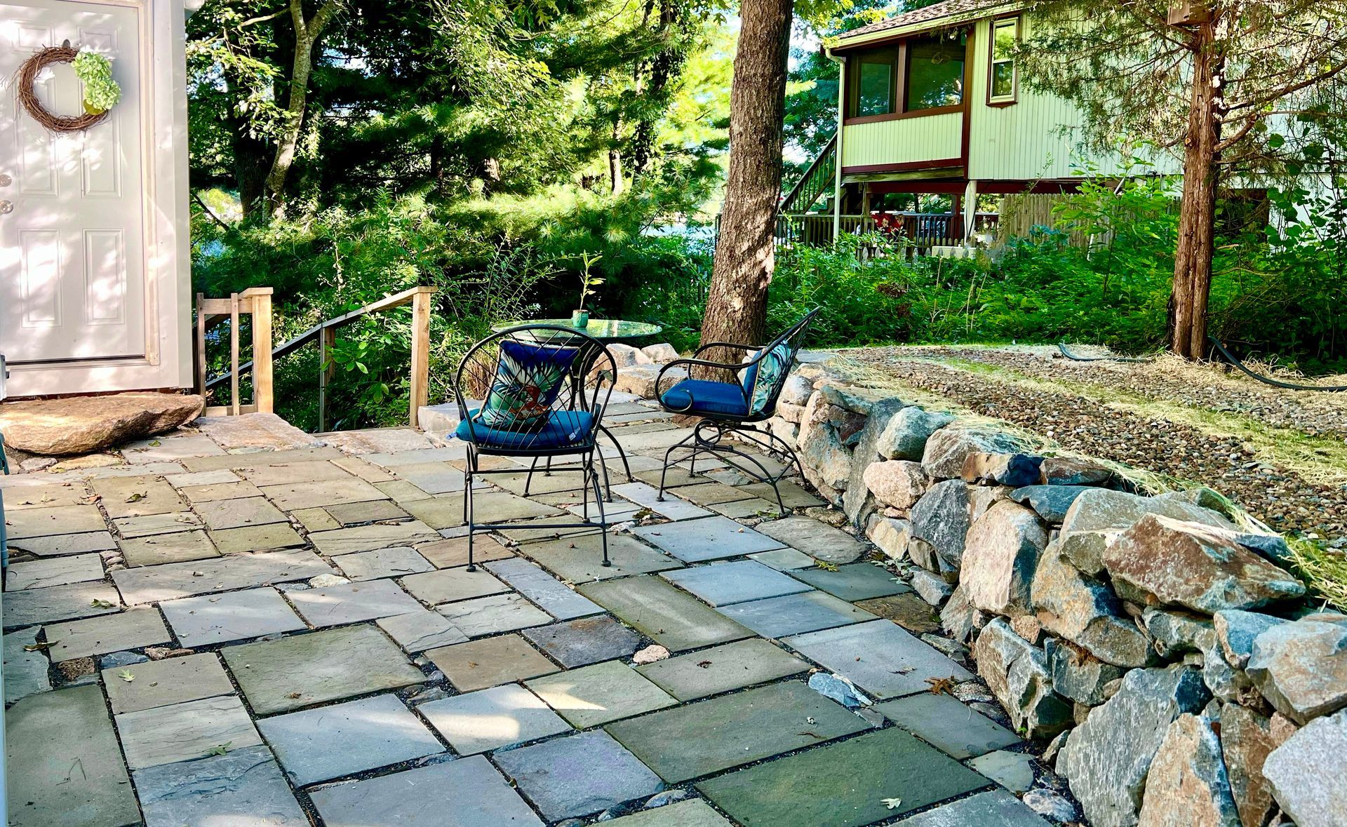 A patio with a stone wall and chairs in front of a house.