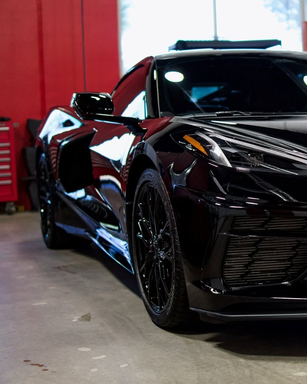 A black sports car is parked in front of a red wall
