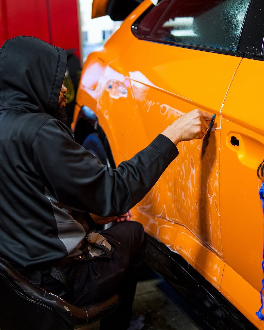 A man in a black jacket is working on an orange car