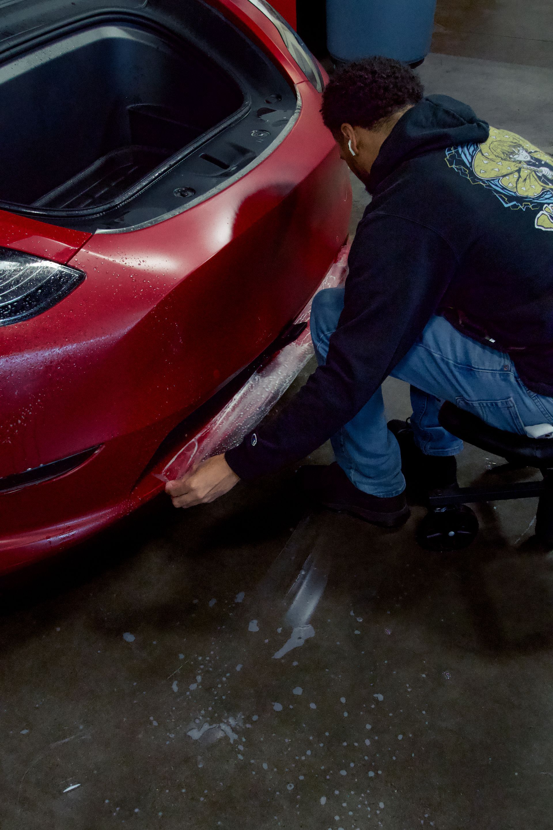 A man is kneeling down next to a red car.
