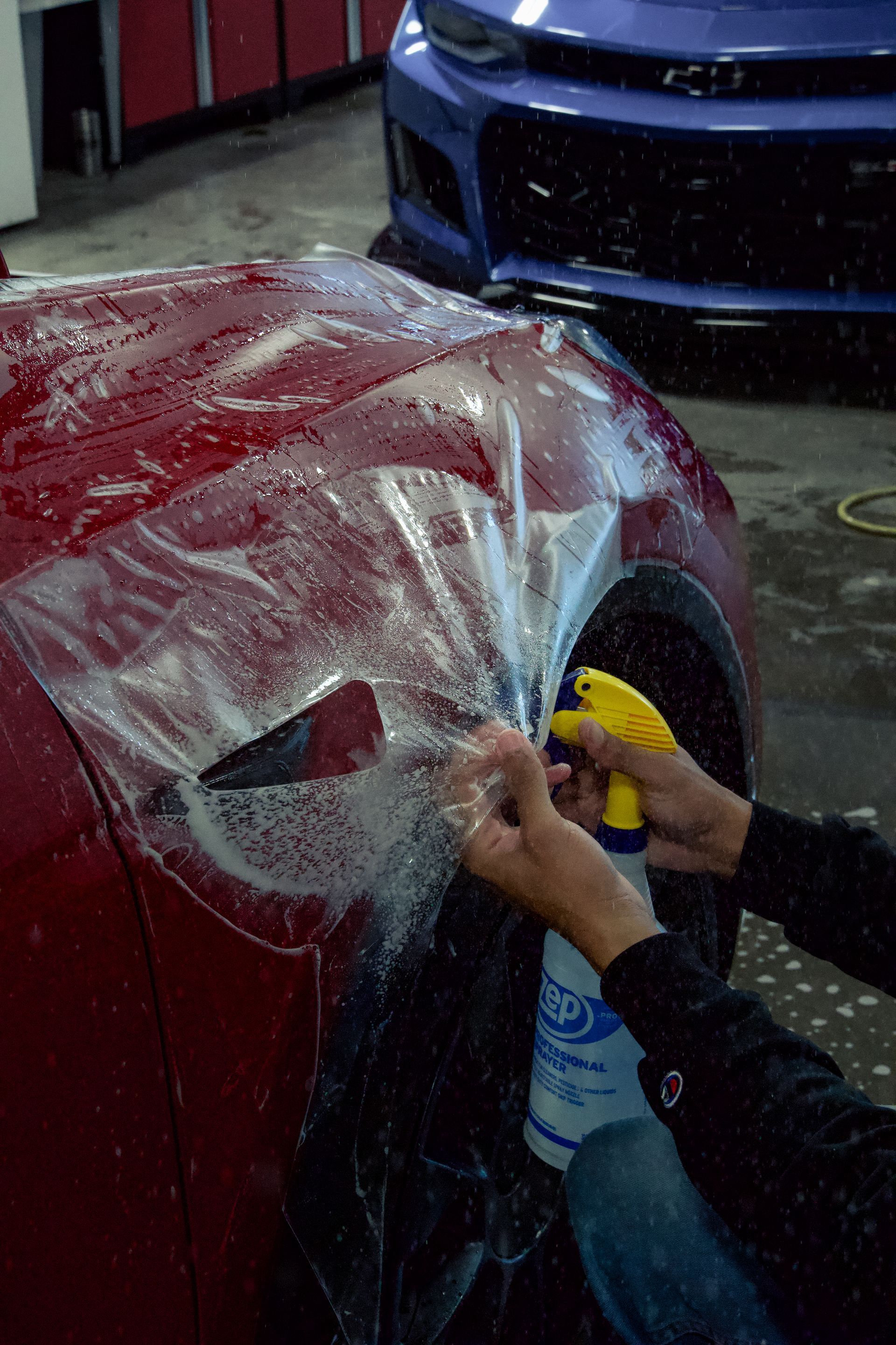 A person is applying protective film to the hood of a red car.