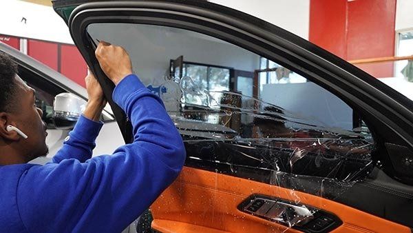 Person applying window tint to a car. Interior with orange trim and red wall in the background.