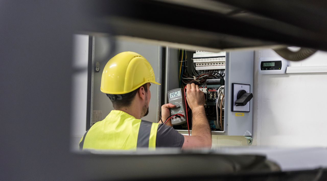 A man wearing a hard hat and safety vest is working on an electrical box.