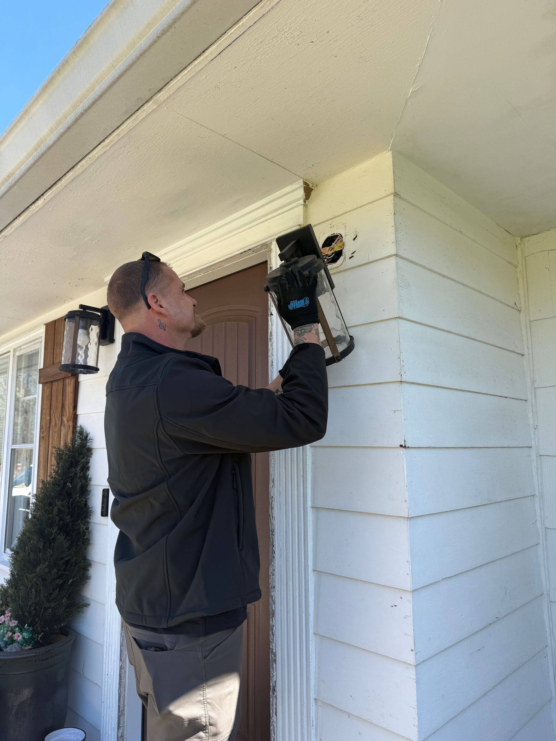 Garden at night lit by a rectangular pillar lamp, surrounded by shrubs, mulch, and grass.