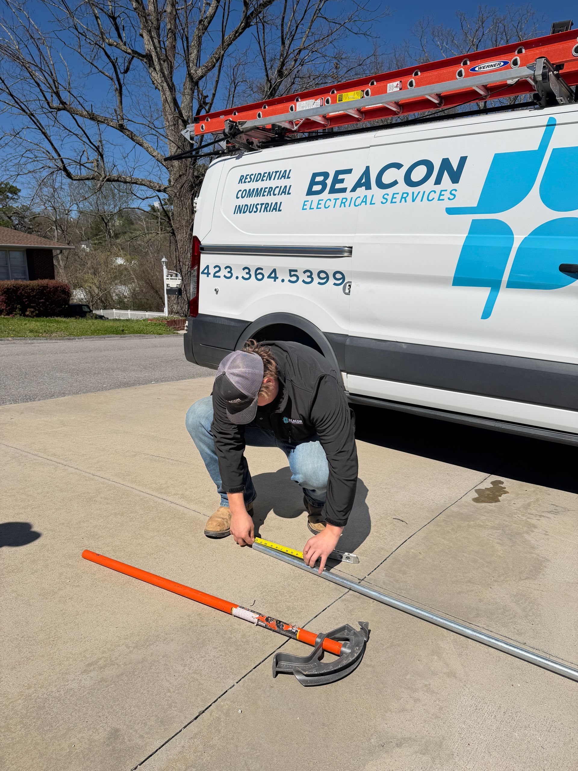 A person kneeling in a grassy field uses a level to install a vertical metal pole into the ground under a blue sky.