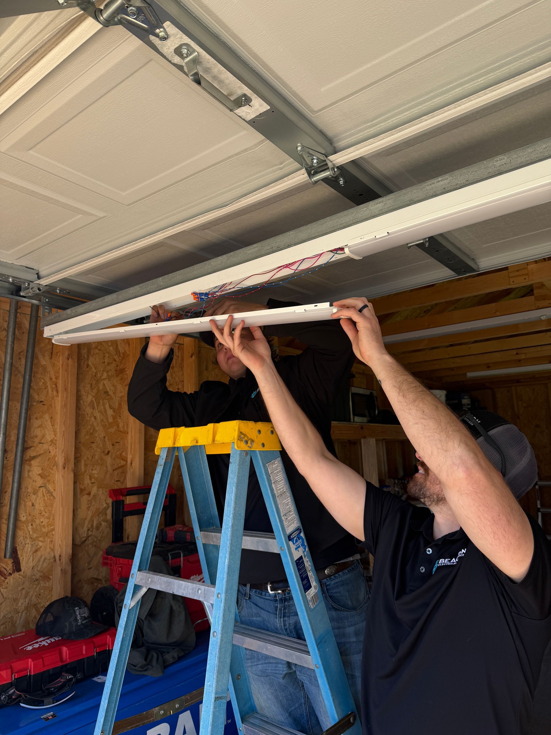 Electrician in blue jumpsuit kneels, working on an outlet in a modern kitchen.