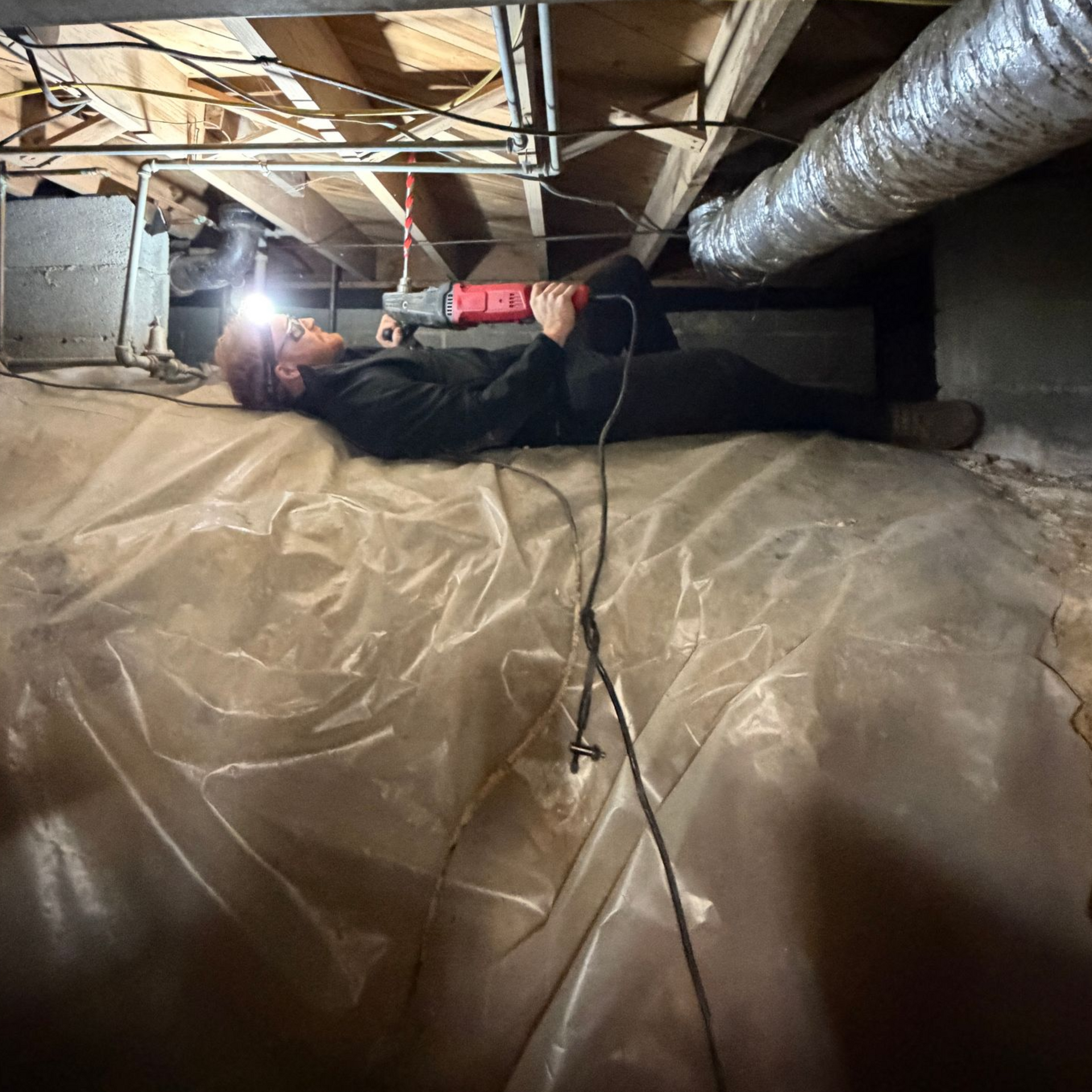 Man in cap working on electrical panel in a dimly lit utility room with exposed wires.
