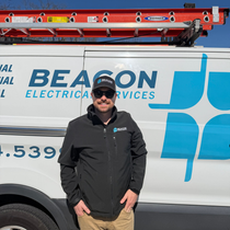 Man in cream sweater shaking hands with a person, indoors at a desk with a laptop and coffee cups.