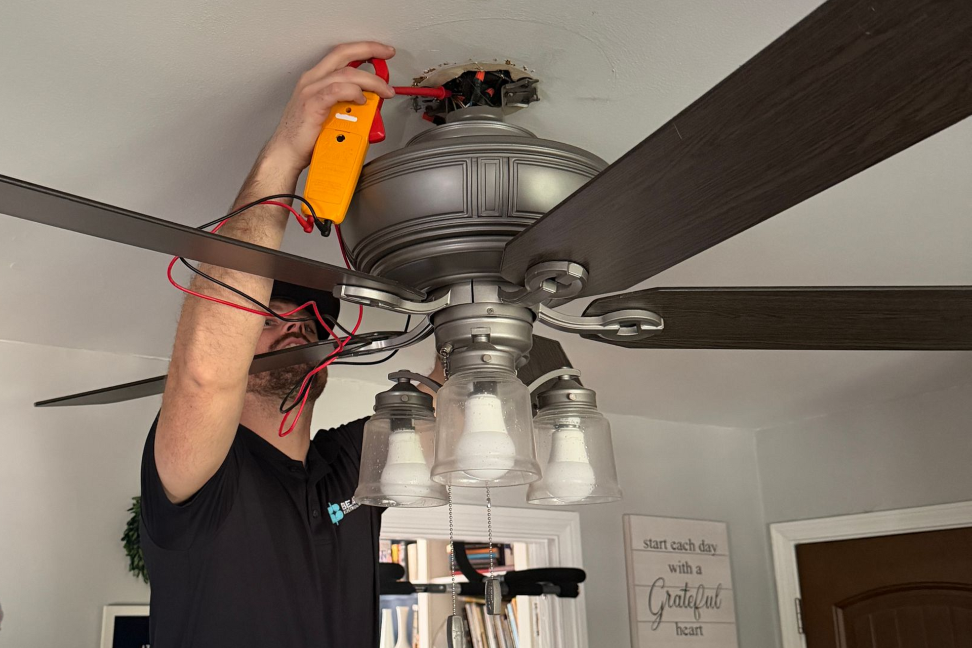 Hand holding tool near electrical panel, with colorful wires and circuit breakers.