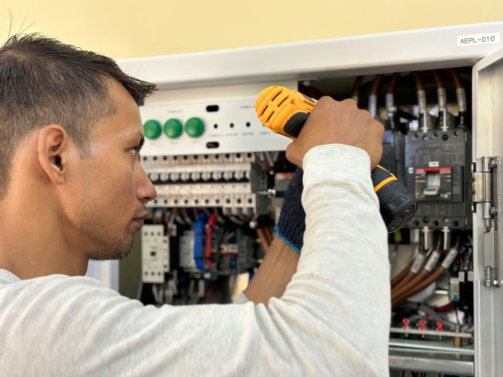 Electrician using a power tool to work on electrical panel.