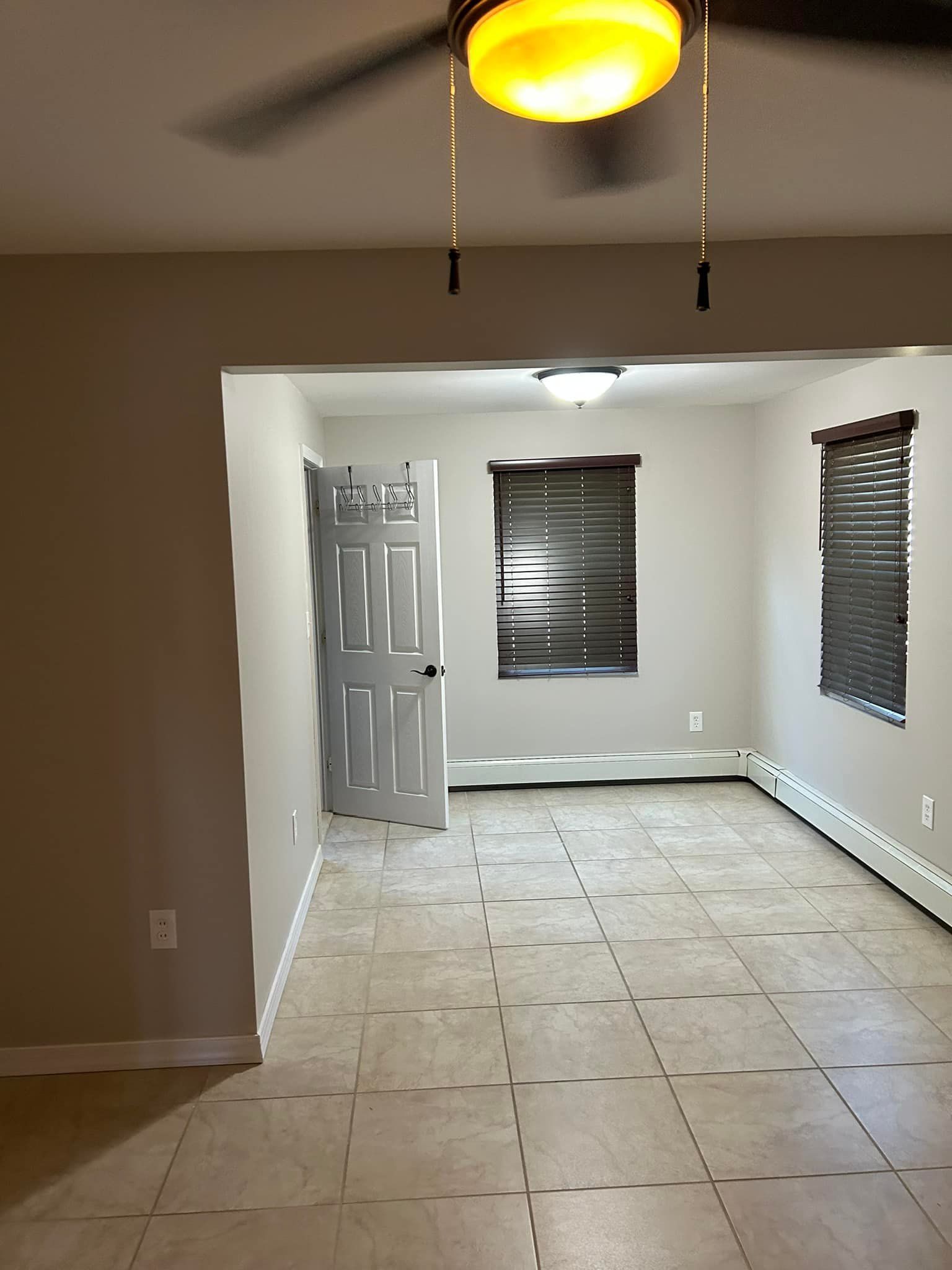 An empty living room with a ceiling fan and blinds.