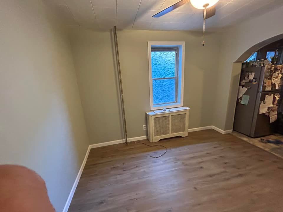 An empty room with a ceiling fan and a refrigerator.