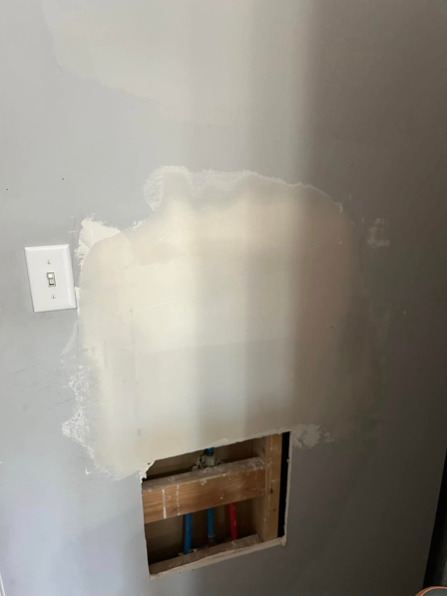 A wall with a hole in it and a light switch.