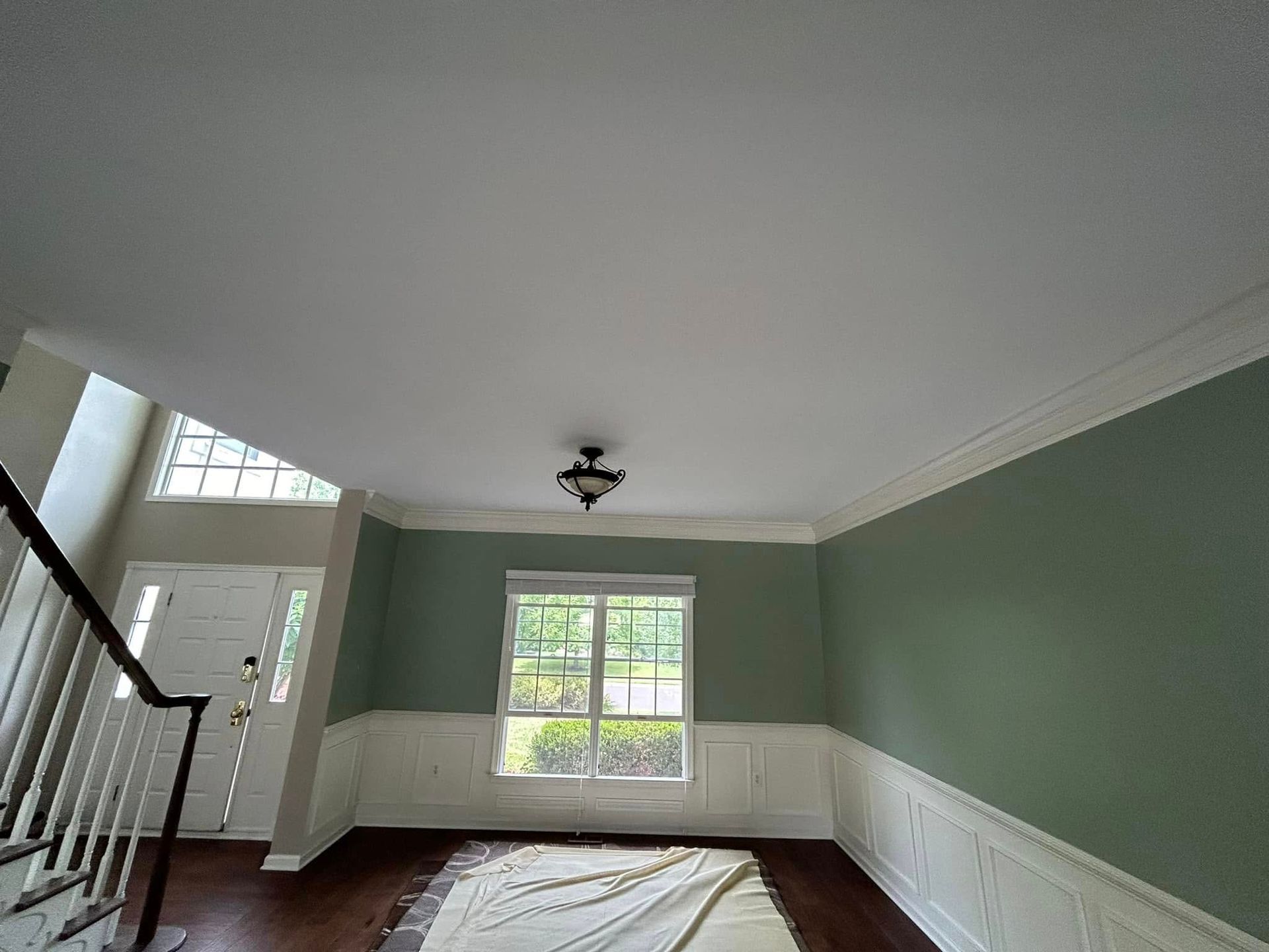 A living room with green walls and white trim is being painted.
