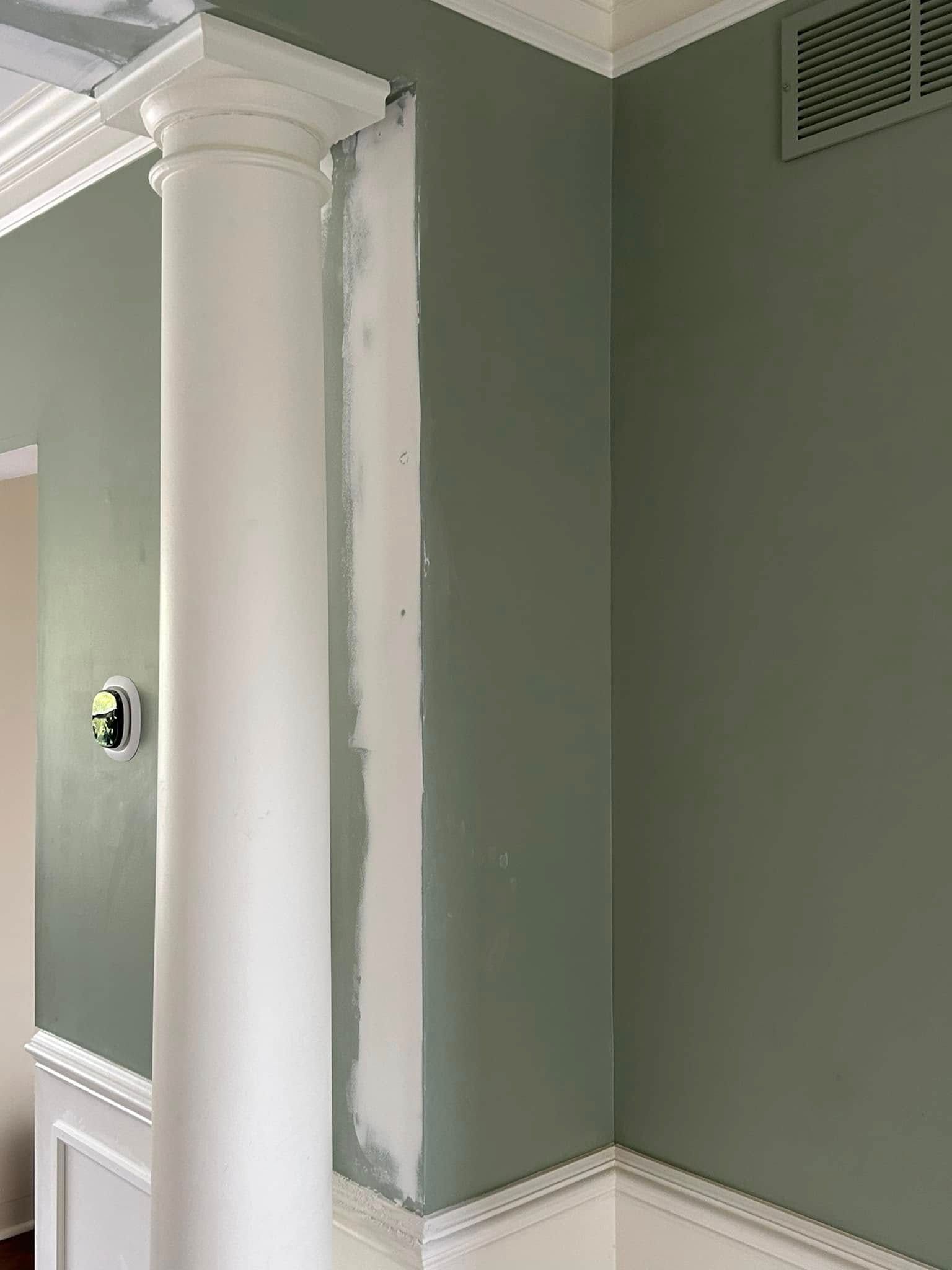 A corner of a room with a white column and green walls.