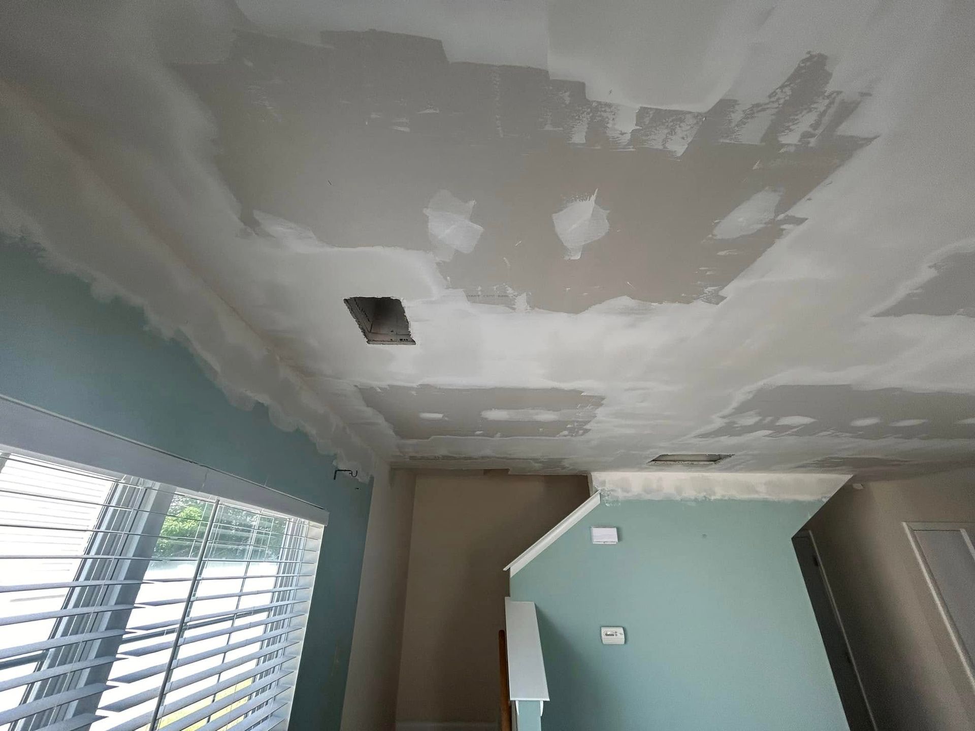 A room with a ceiling that is being painted and a window.