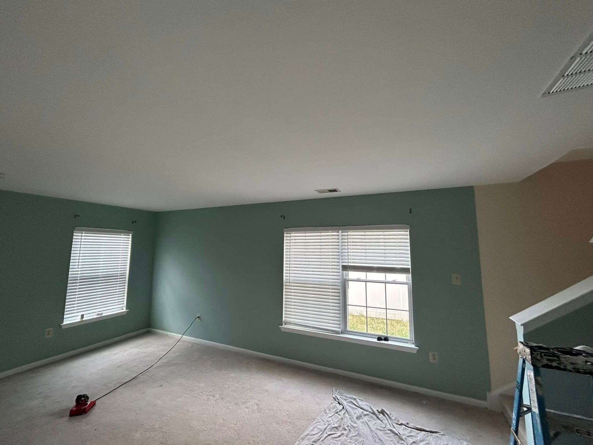 An empty living room with two windows and a ladder