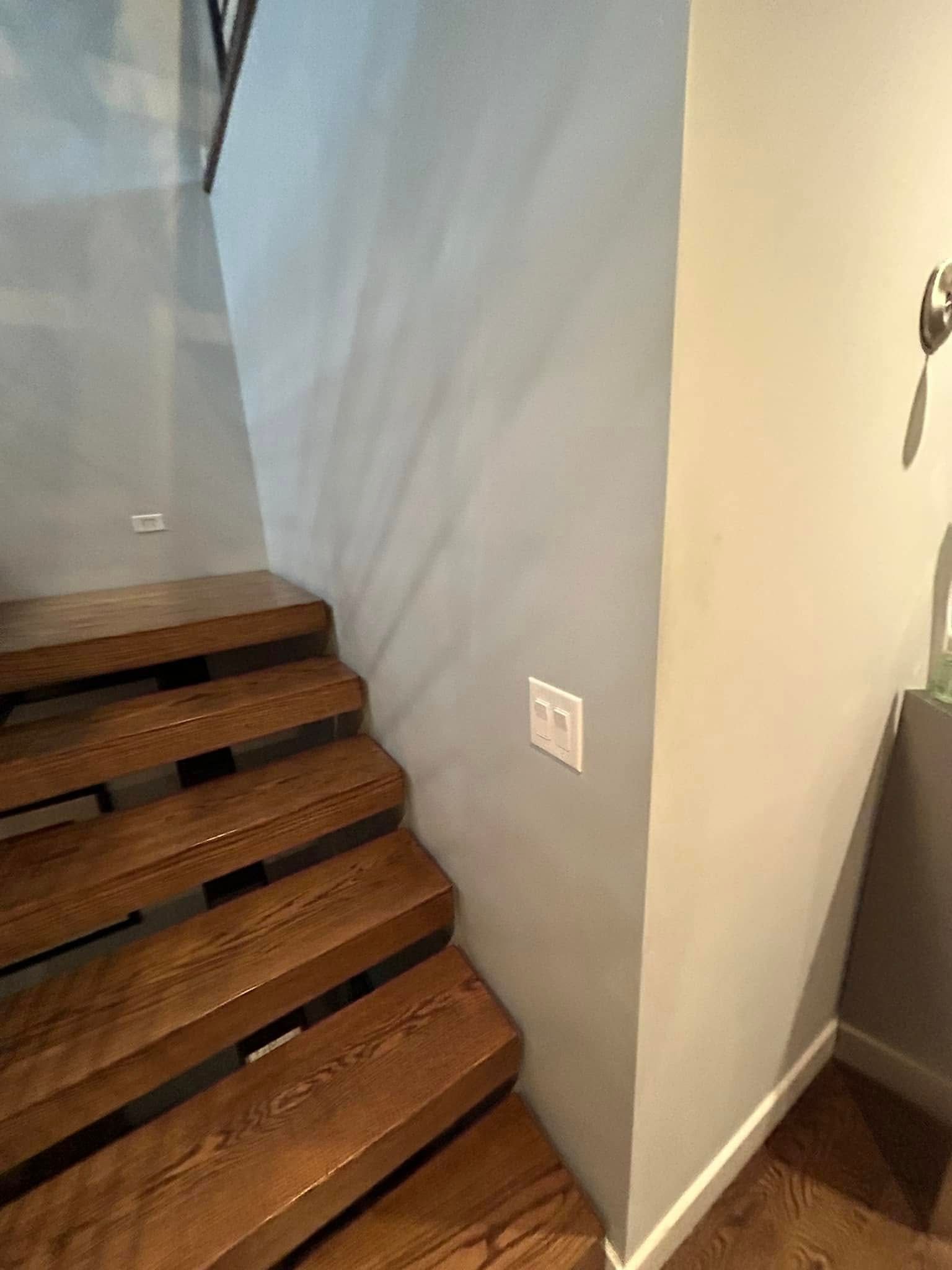 A wooden staircase in a room with a light switch on the wall.