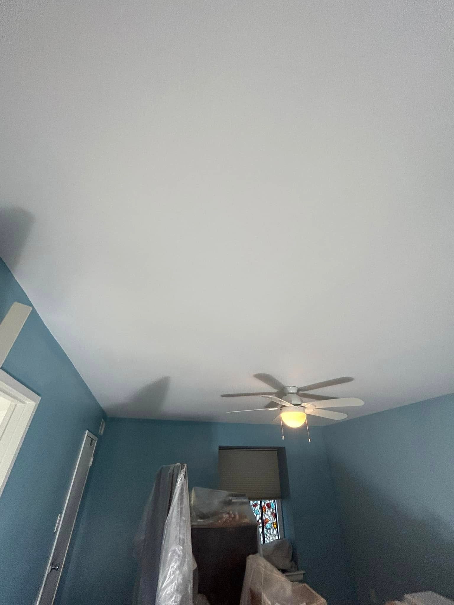 A bedroom with blue walls and a white ceiling fan.