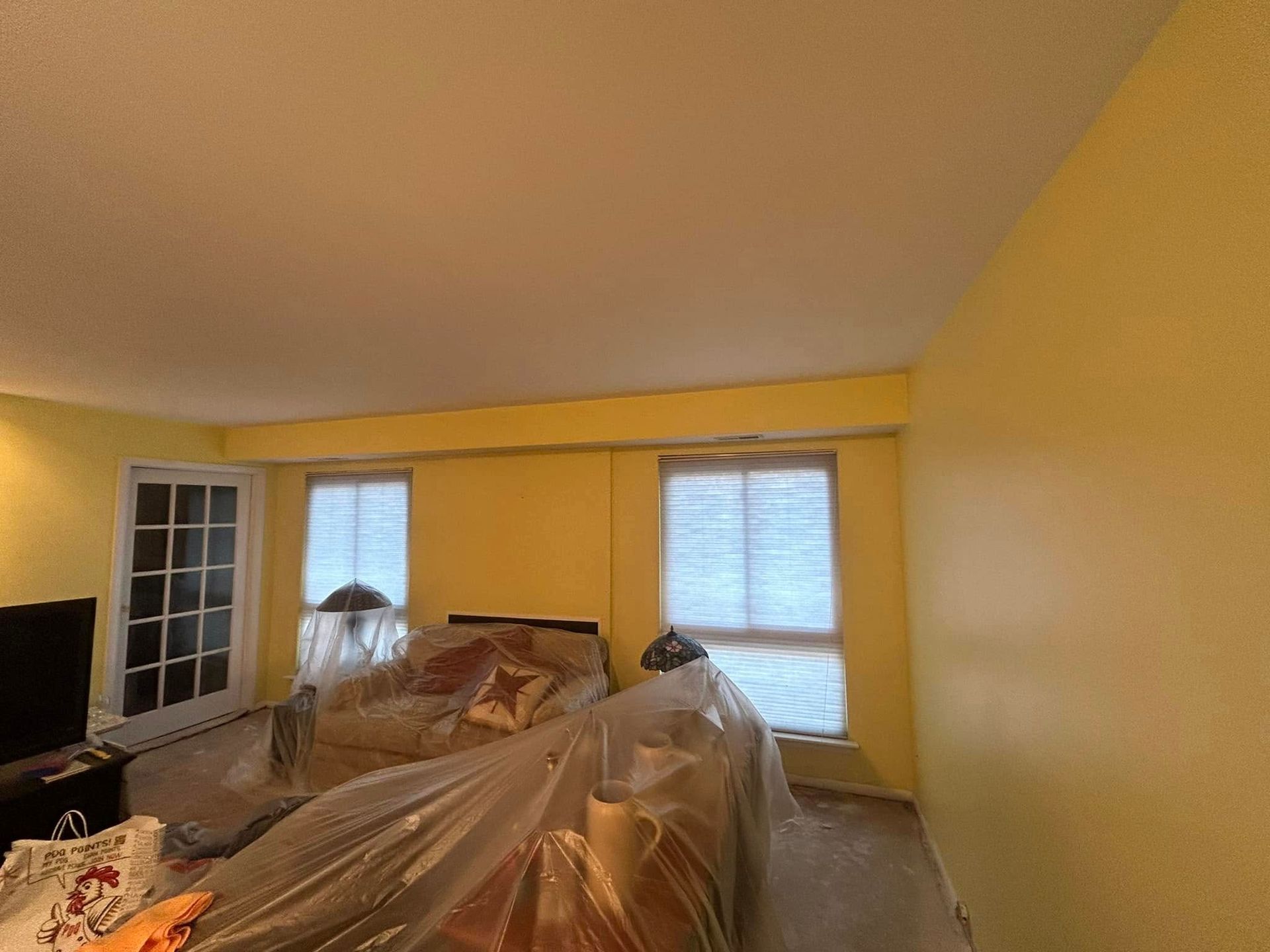 A living room with yellow walls and a couch covered in plastic.