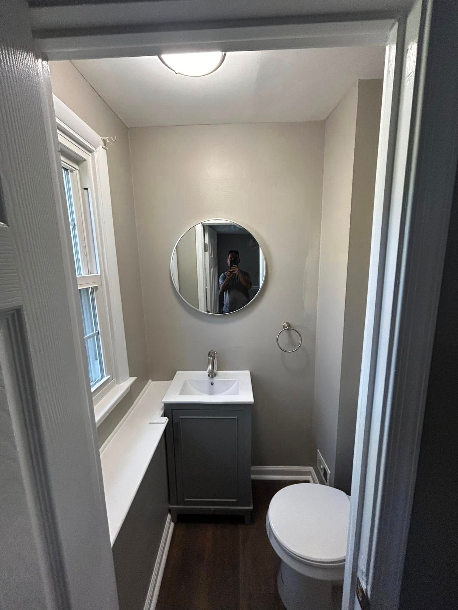 A bathroom with a sink , toilet , mirror and window.