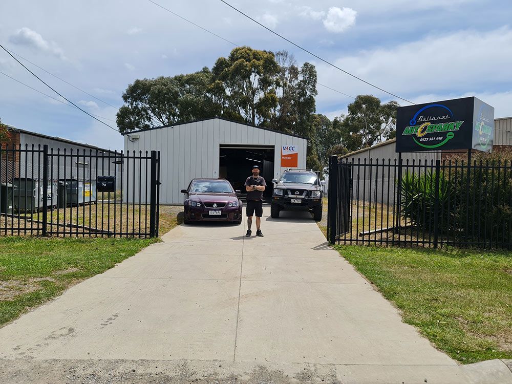 A Man Is Standing In Front Of A Garage With Two Cars Parked In Front Of It — Ballarat Auto Sparky in Sebastopol, VIC