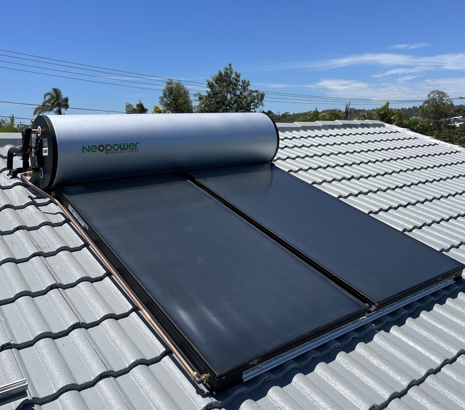 Solar hot water system on a tiled roof with a blue sky background.
