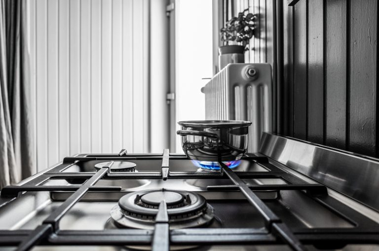 Gas stove with pot on the burner, blue flame, in a kitchen with white and dark walls.