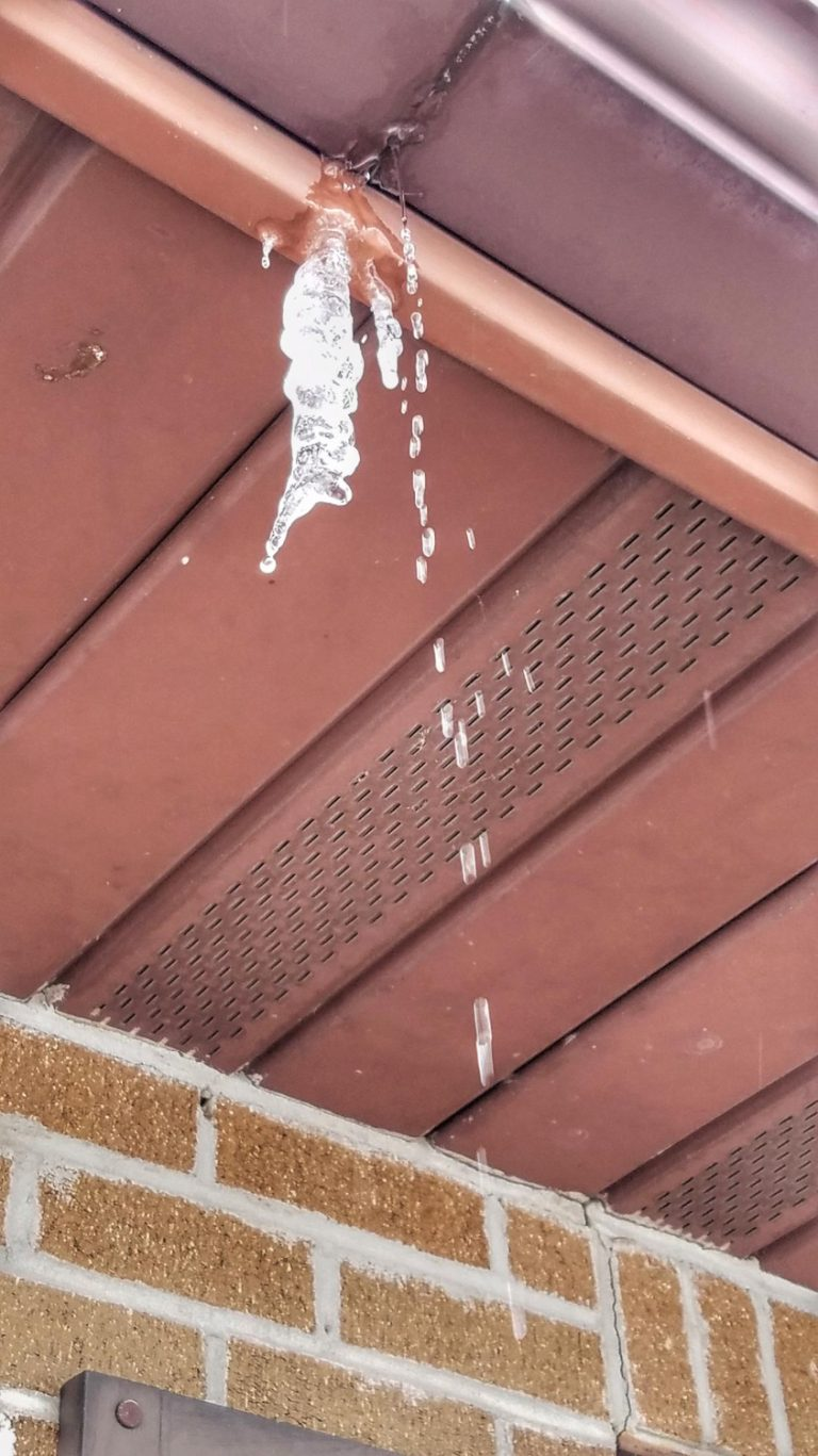Icicles hanging from a brown soffit on a brick building.