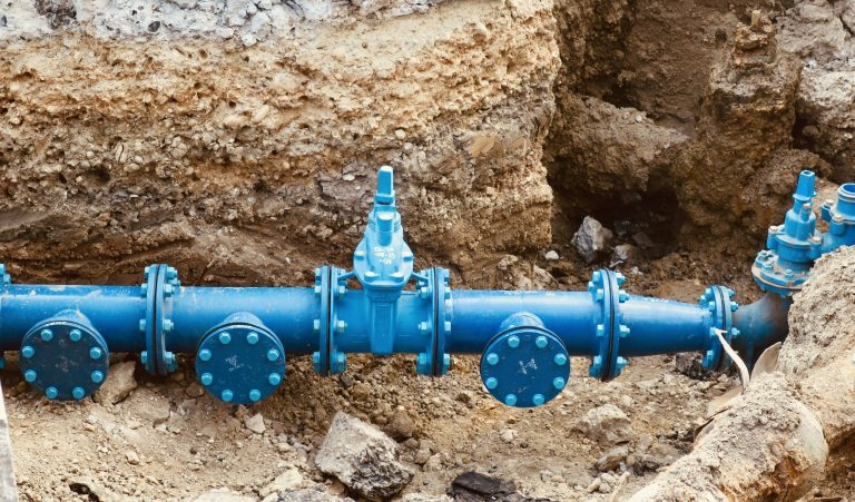 Blue water pipes with valves buried in dirt.
