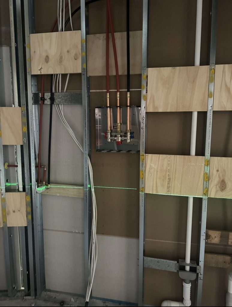 Construction site interior with plumbing and electrical work in a wall frame.