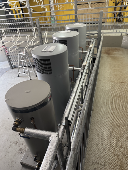 Four gray water heaters in an industrial setting, next to a metal railing.
