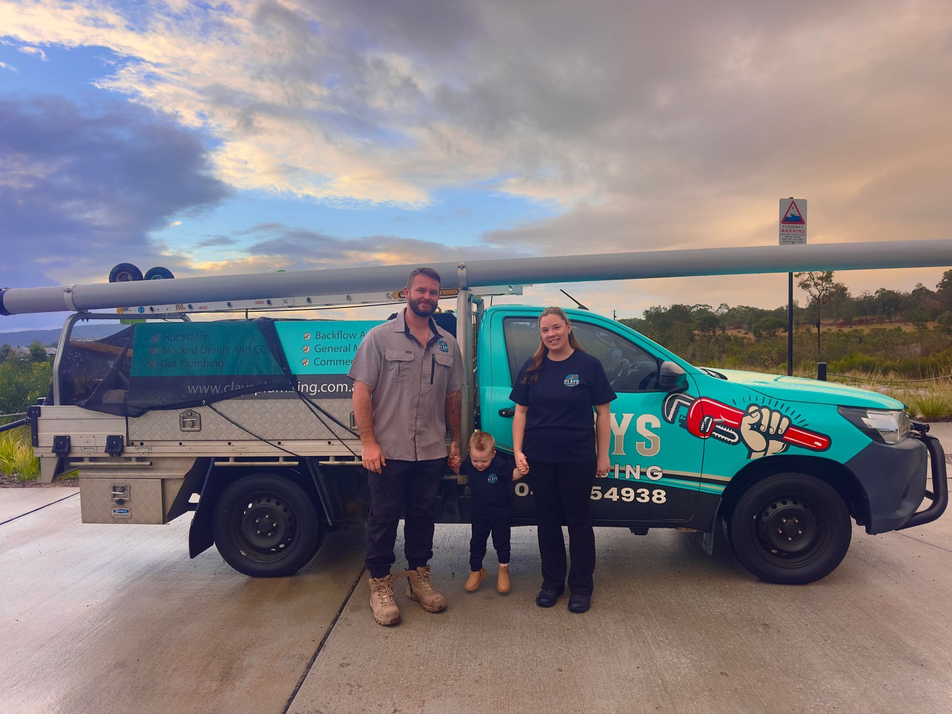 A teal plumbing truck parked near a beach. It has pipes on top and a logo on the side.