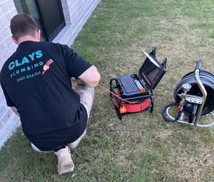 Plumber using a camera to inspect a pipe next to a building. He is wearing a black shirt.