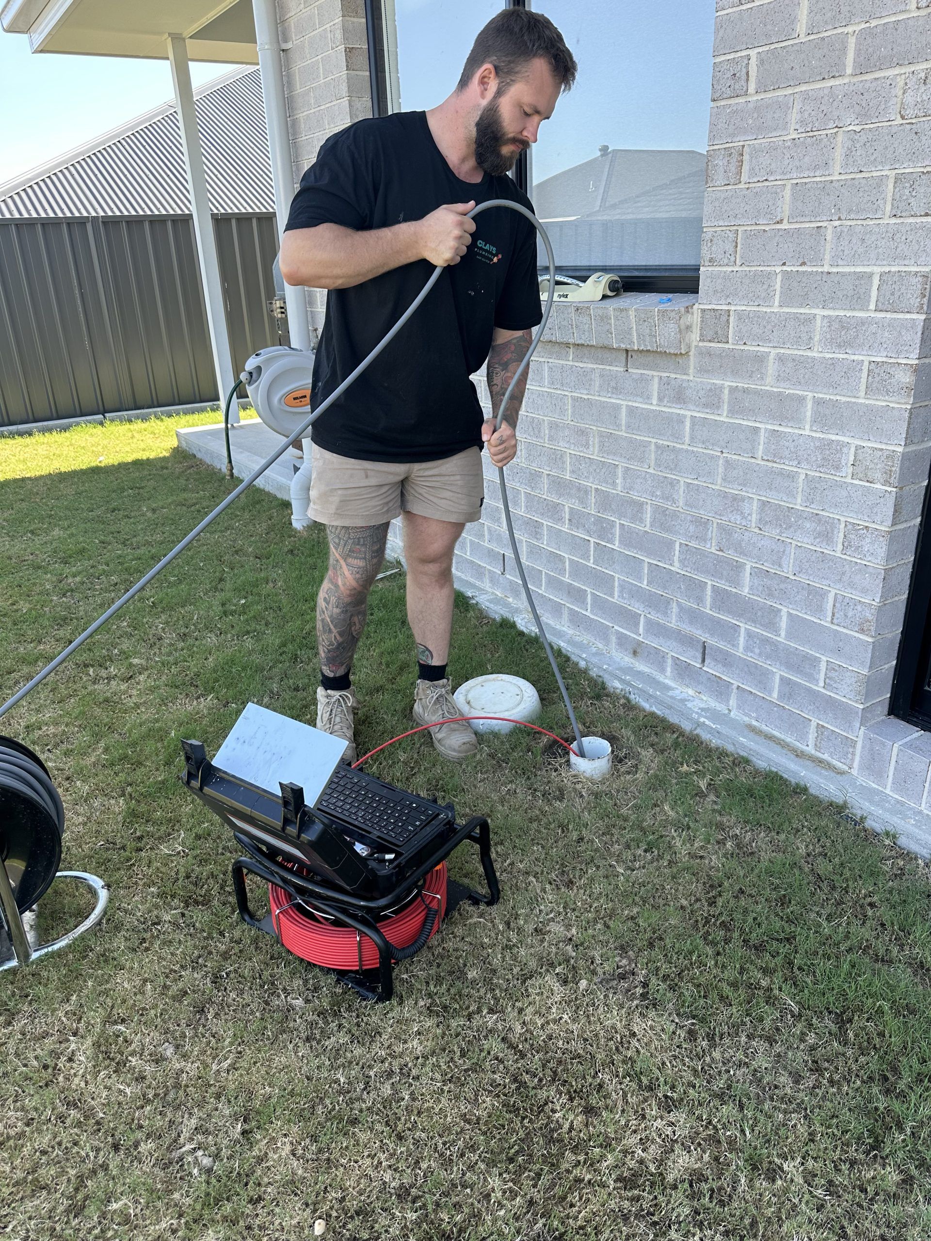 Man using drain cleaning equipment outdoors near a brick building.