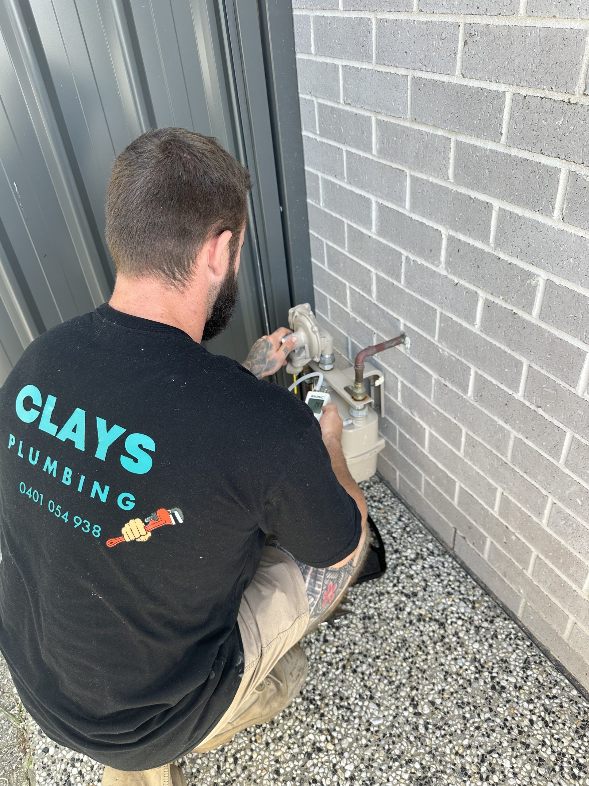 Plumber working on gas meter near a brick wall and corrugated metal.
